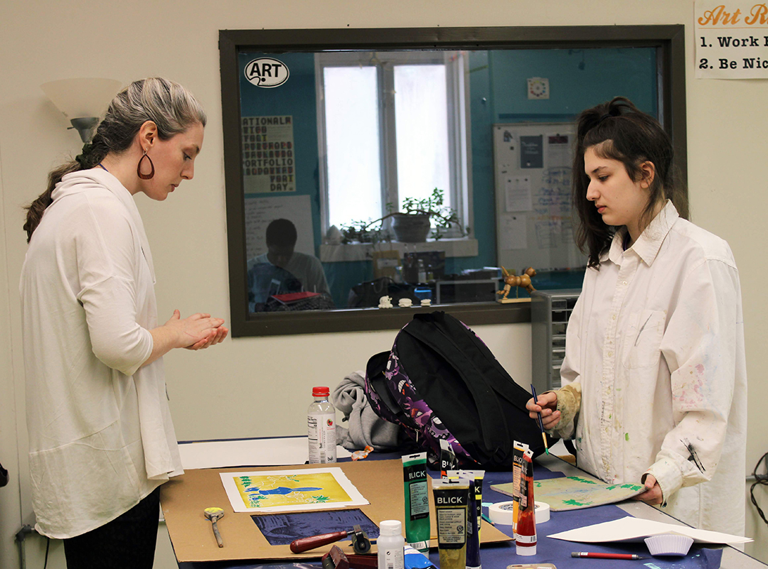 Two people stand at opposite sides of a desk.